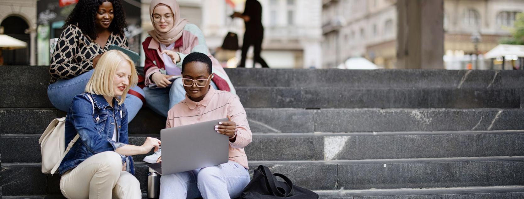 A diverse group of college women sit on outdoor stairs on campus.